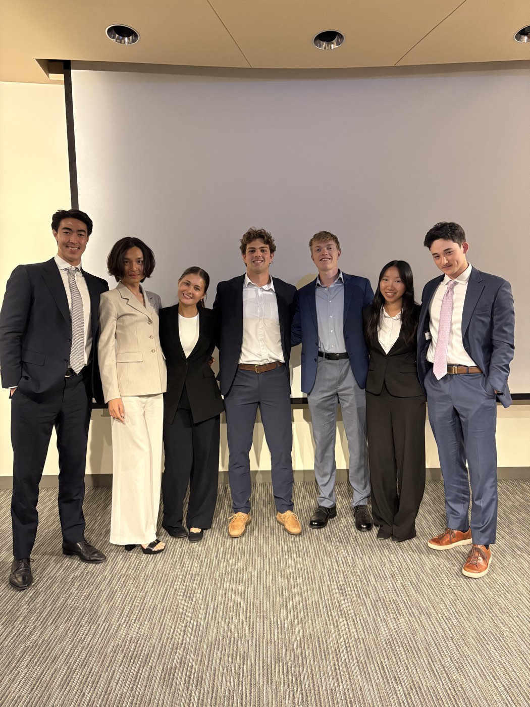 Minh, second from left in a beige suit, with six members of the Magnetar summer team in a presentation room.