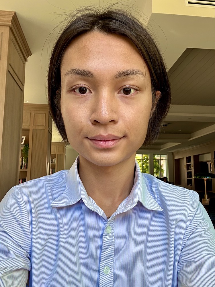 Close-up of Minh in a blue-striped oxford shirt, with a calm expression.